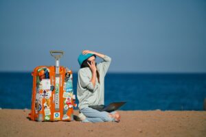 Woman with a laptop and suitcase on a tropical beach, ready to start her digital nomad journey in Southeast Asia